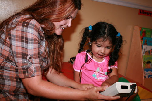 a woman showing an hearing screening device to a smiling girl